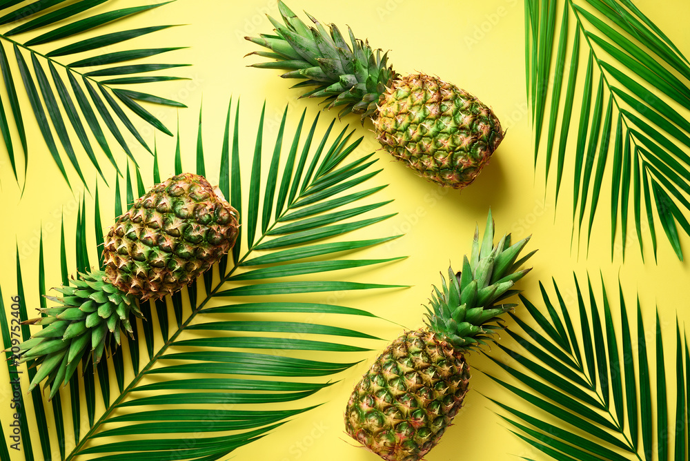 Pineapple and tropical palm leaves on yellow background. Top view. Summer concept. Creative flat lay with copy space. Pineapple and tropical palm leaves on yellow background. Top view. Summer concept. Creative flat lay with copy space.