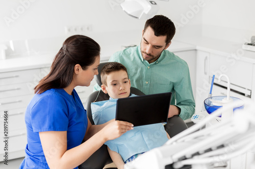 medicine  dentistry and healthcare concept - dentist showing tablet pc computer to kid patient and his father at dental clinic