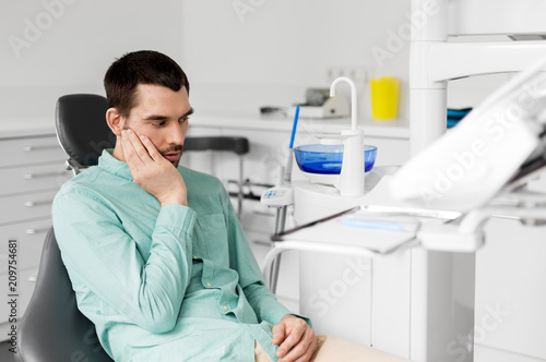 medicine, dentistry and healthcare concept - male patient suffering from toothache at dental clinic office