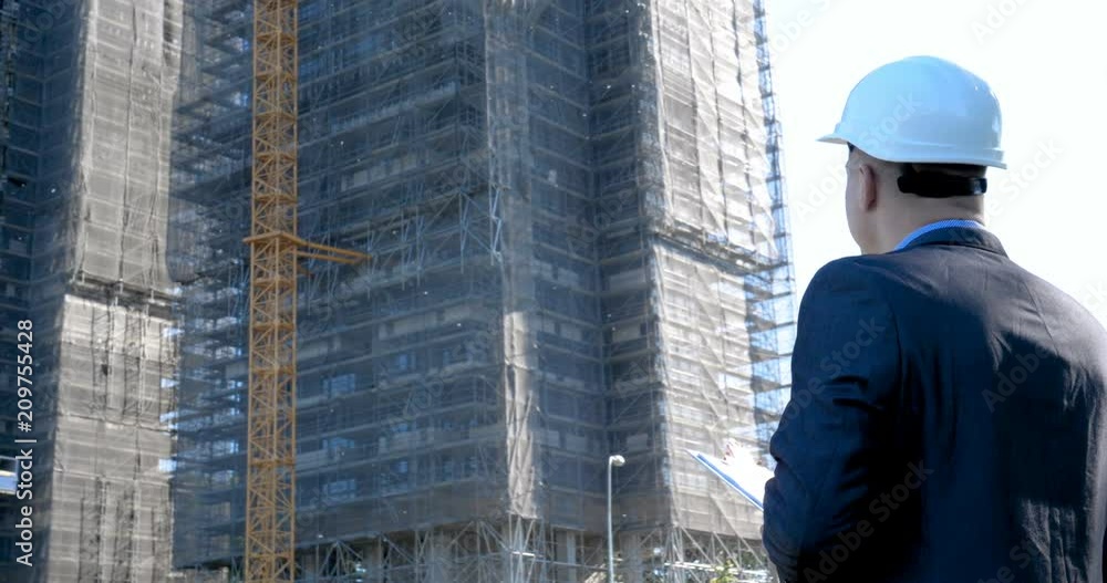 Portrait of a successful young handsome engineer, architect, builder, businessman, wearing a white helmet, in a suit, holding a notepad, skyscraper background and building. Portrait of a successful young handsome engineer, architect, builder, businessman, wearing a white helmet, in a suit, holding a notepad, skyscraper background and building.