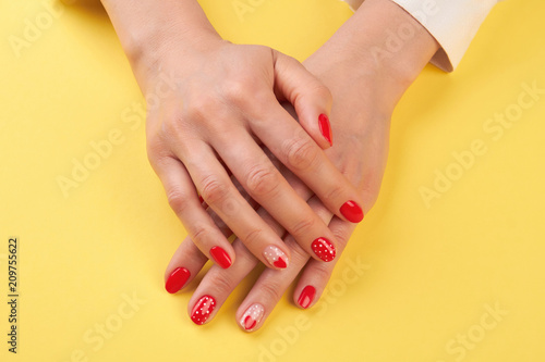 Manicured hands isolated on yellow background. Woman hands with natural nails polished with red varnish. Female well-groomed hands isolated on yellow background.