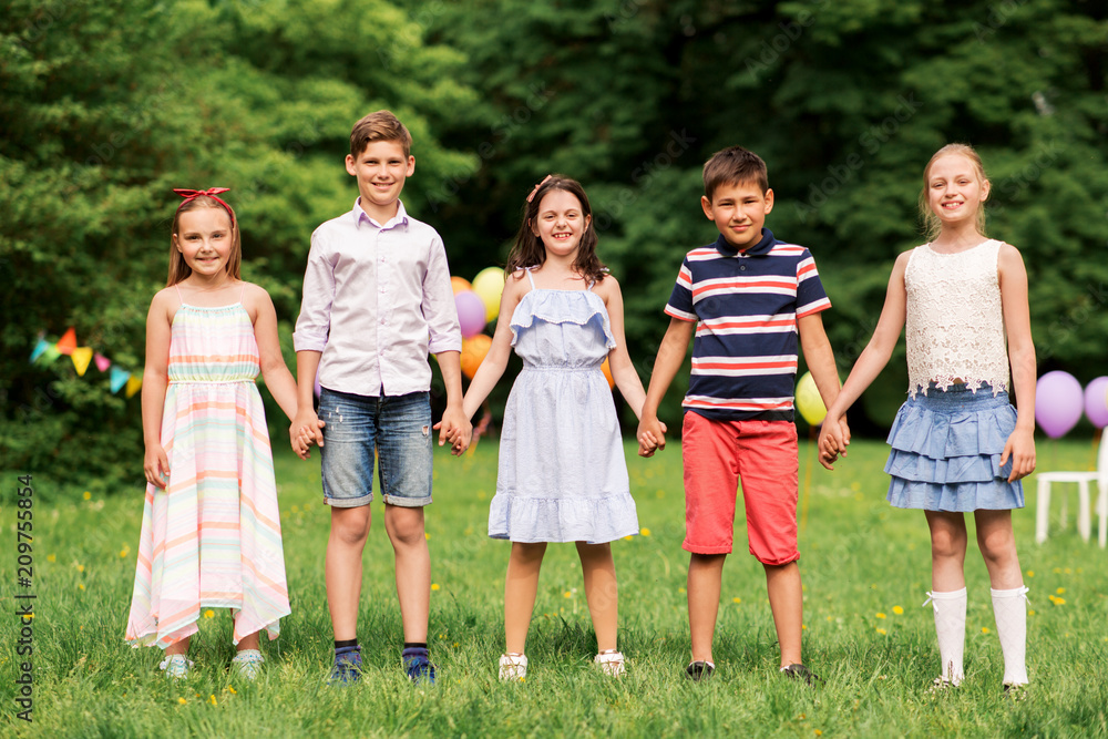 holidays, childhood and celebration concept - happy kids holding hands on birthday party at summer park holidays, childhood and celebration concept - happy kids holding hands on birthday party at summer park