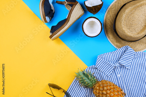 Summer vacation flatlay with straw hat, espadrilles, coconut halves, body oil, stripped dress and glasses on blue and yellow with copyspace