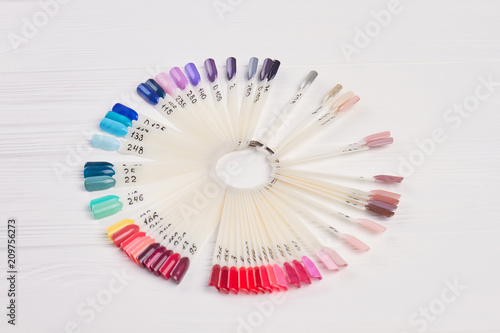 Big variety of nail color samples. Manicure nails polish color on white wooden background. Nail beauty studio.