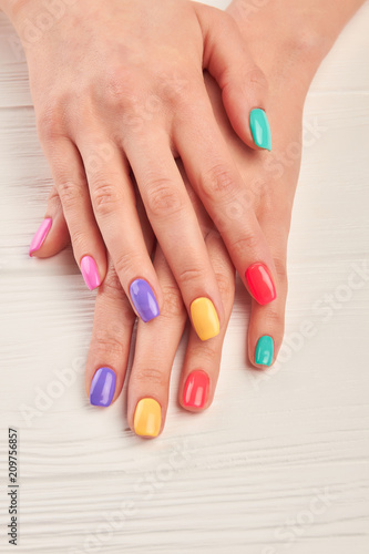 Well-groomed hands with summer manicure. Young woman nails covered with different colors polish on white wooden background. Perfect summer manicure.