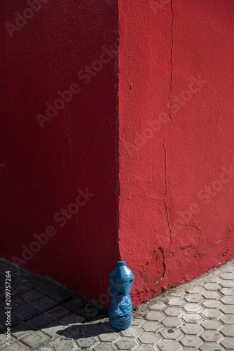 Minimal vanguardism picture of a crumpled blue bottle over a corner of a red wall photo