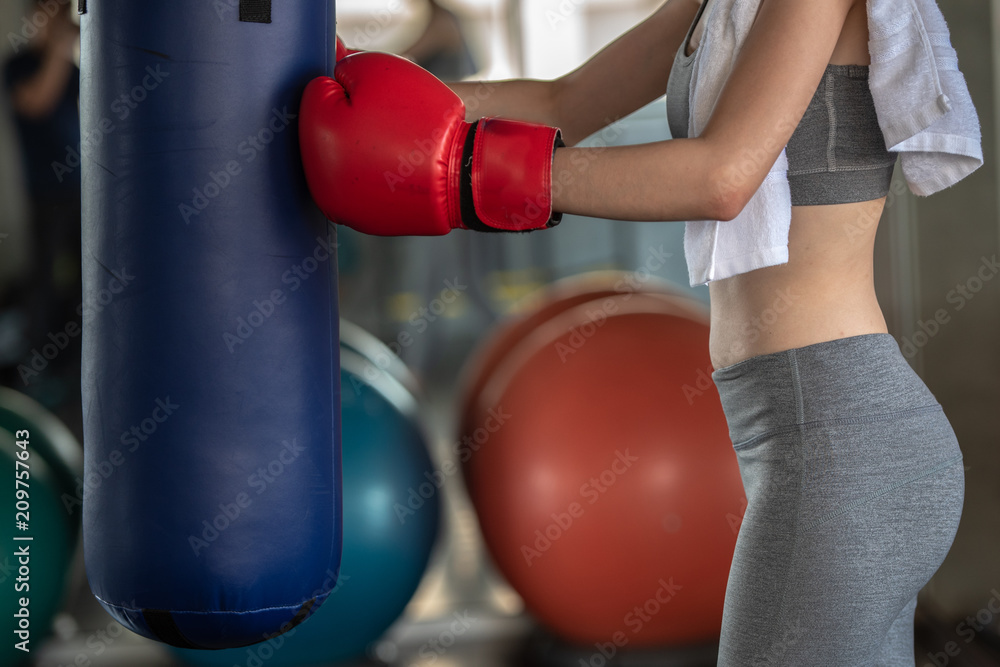 Portrait photo about  body of cute Asian sports girl in red boxing gloves and big punching bag at indoor sport gym, beauty and healthy sport concept.