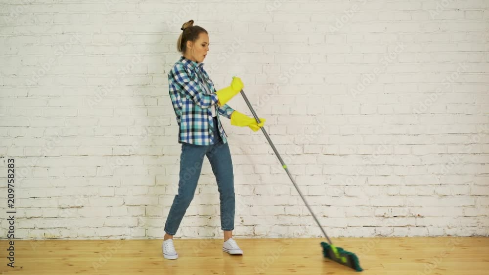 Beautiful young woman is dancing and smiling while cleaning floor at home using a mop Beautiful young woman is dancing and smiling while cleaning floor at home using a mop
