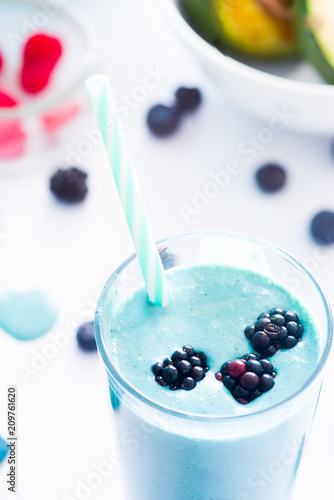 Blue Majik smooothie on tall glass with colored straw, over a blue colored wooden board against a clear background
