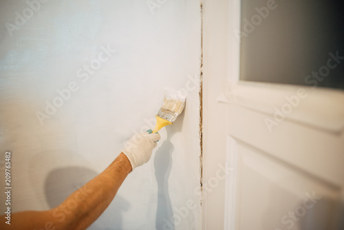 A man's hand with a brush with white door paint. Selected focus