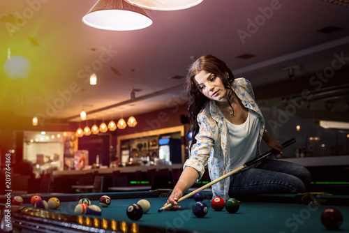 Woman sitting on billiard table going make a hit photo