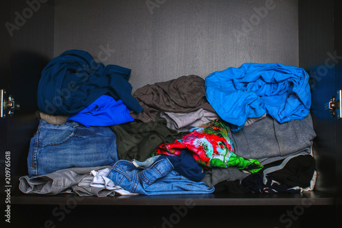 A pile of different clothes is lying on the shelf in the closet.