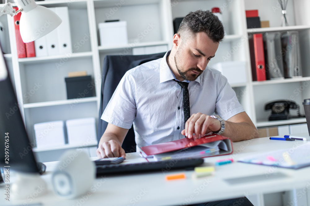 A man sits at a table in the office and looks at the wristwatch. A man sits at a table in the office and looks at the wristwatch.