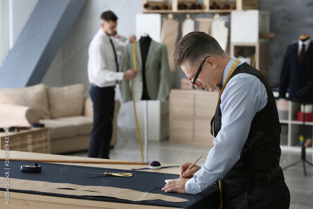 Mature tailor and his assistant working in atelier Mature tailor and his assistant working in atelier