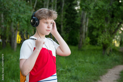 Boy in headphones listens to music. Teenager in headphones in the forest