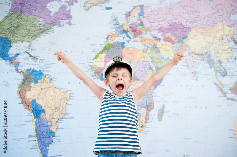 Obraz premium happy shouting little kid in captain hat and striped shirt world map background