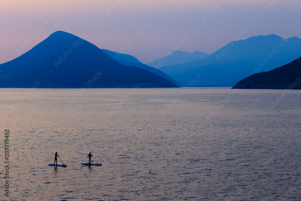Two serfer silhouettes in front of mountains in sunset, Montenegro