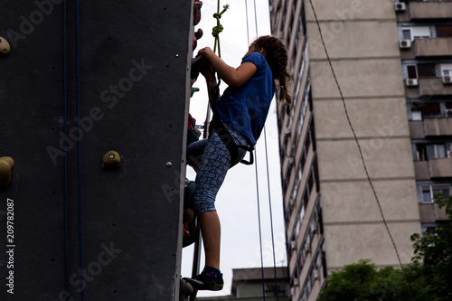 Beautiful young girl climbing to big artificial wall