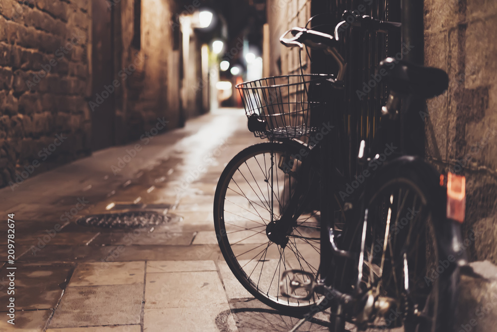 retro bicycle in the night old city on background bokeh light flare in night architecture, vintage bike in evening street in barcelona town, cycle transportation in defocus backdrop, travel concept