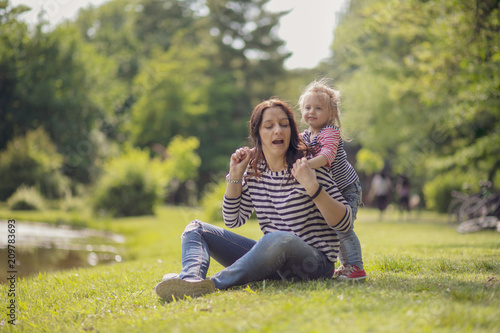 Happy mother and daughter in the park. Beauty nature scene with family outdoor lifestyle. Happy family resting together on the green grass  having fun outdoor. Happiness and harmony in family life