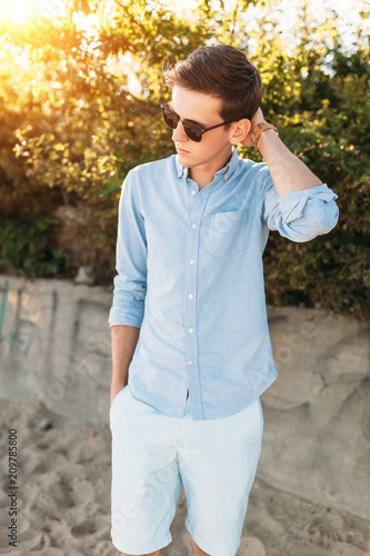 Beautiful stylish guy with glasses, posing on the beach, at sunset, hipster posing in stylish clothes, for advertising, text insertion