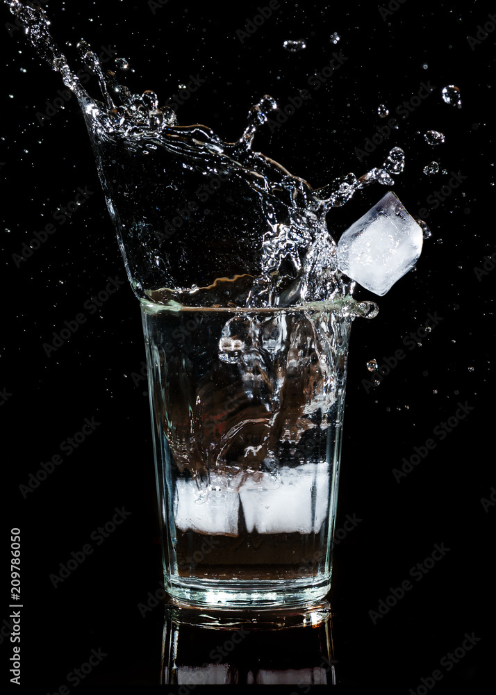 Splash of water with an ice cube in a glass on a black background Splash of water with an ice cube in a glass on a black background
