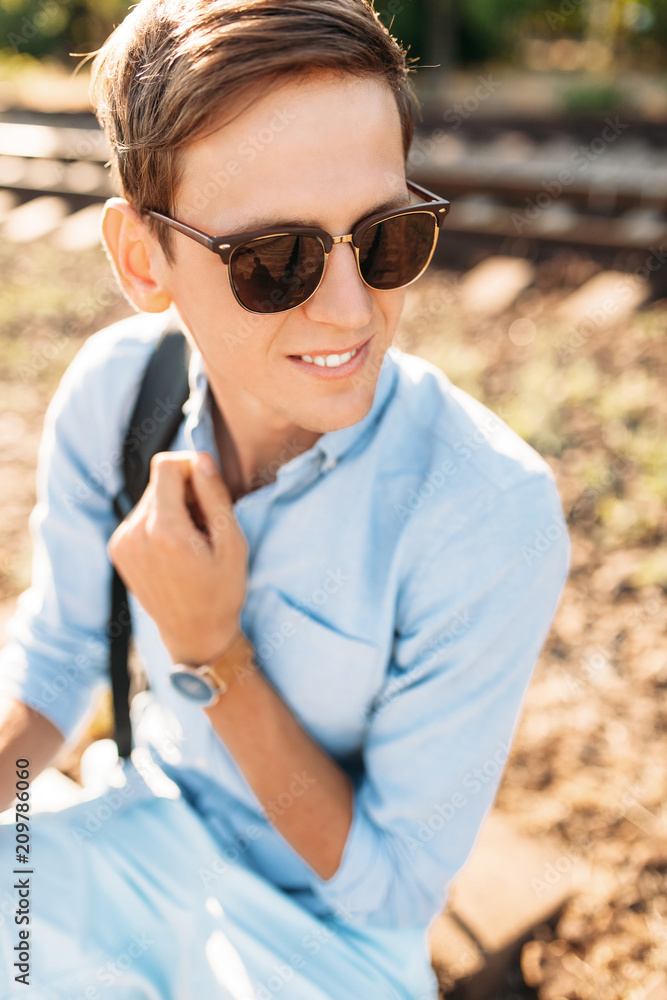 Beautiful stylish guy with glasses, posing sitting on the rails of the train at sunset, hipster posing in stylish clothes, for advertising, text insertion Beautiful stylish guy with glasses, posing sitting on the rails of the train at sunset, hipster posing in stylish clothes, for advertising, text insertion