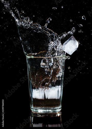 Splash of water with an ice cube in a glass on a black background