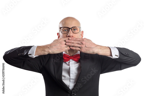 Slim bald elegant nerd in black suit with bow tie gesturing Speak No Evil. Isolated on white.