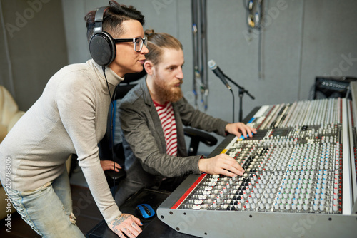 Man and woman working together on music creation standing at electronic board in sound studio. 