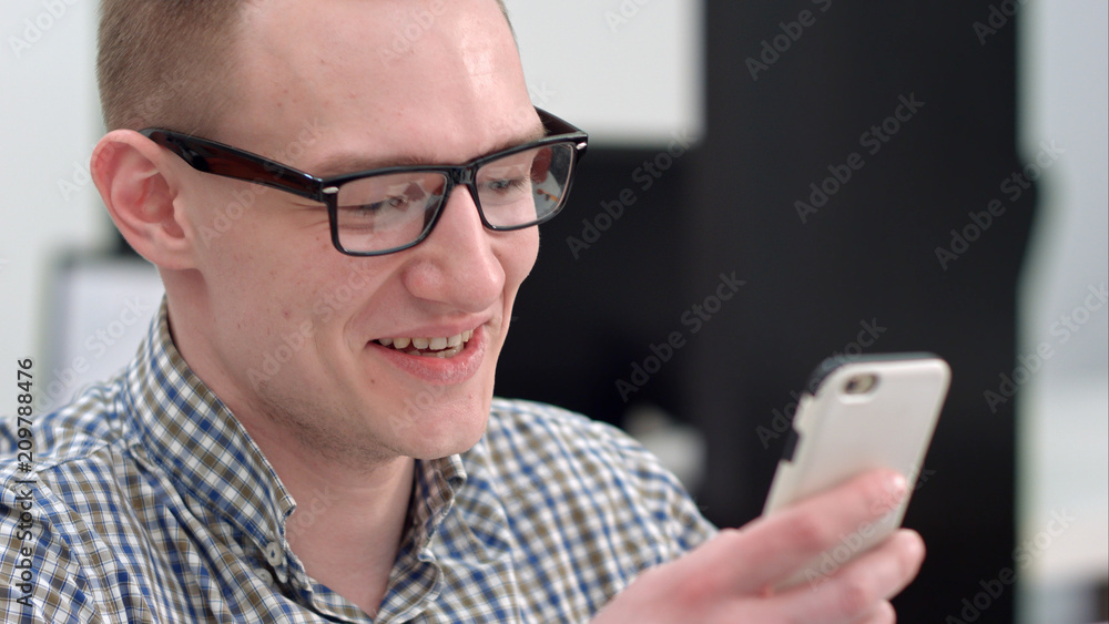 Young man in office laughing at text message on smartphone Young man in office laughing at text message on smartphone