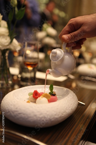 Tableside Service at customer's table by Professional Starred Chef. Pouring over to a luxury fine dining dessert in white stylish bowl. Final touch to perfect meal. Selective focus. Bokeh background. 