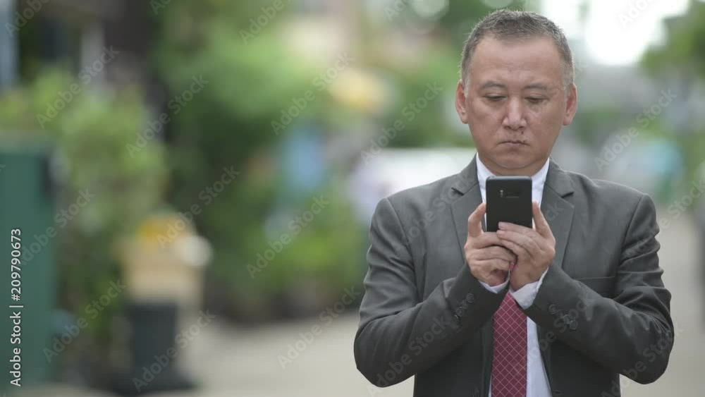 Mature Japanese businessman using phone in the streets outdoors Mature Japanese businessman using phone in the streets outdoors