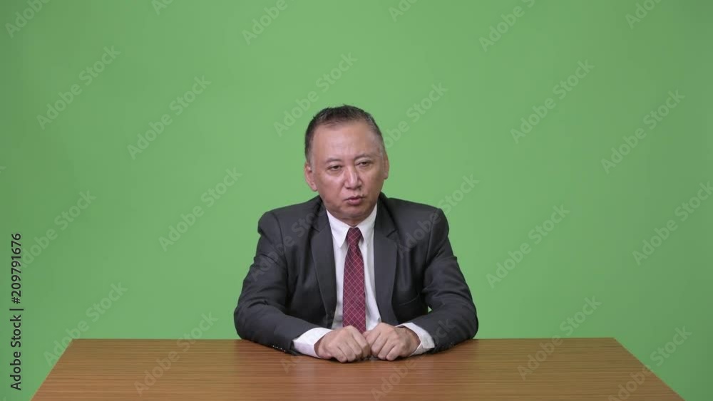 Mature Japanese businessman talking against green background Mature Japanese businessman talking against green background