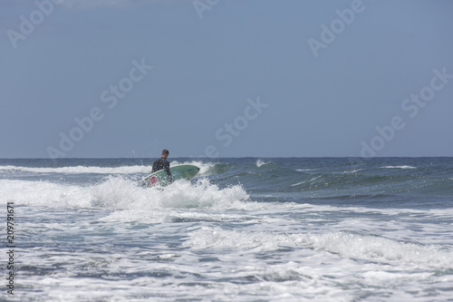 The surf enters the water. Male surfer entering the sea with his board in a black surfing suit. Tenerife, Spain. Surfer entering the ocean .Ready for a great surfing day.