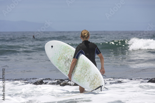 The surf enters the water. Male surfer entering the sea with his board in a black surfing suit. Tenerife, Spain. Surfer entering the ocean .Ready for a great surfing day.