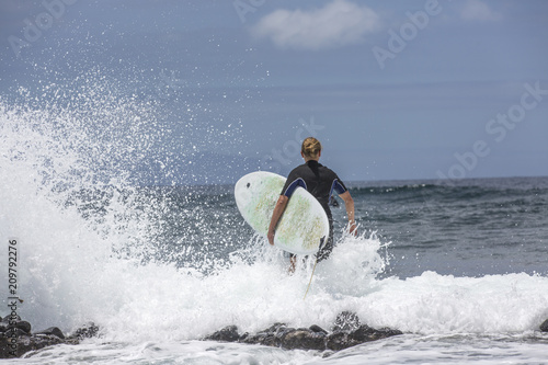 The surf enters the water. Male surfer entering the sea with his board in a black surfing suit. Tenerife, Spain. Surfer entering the ocean .Ready for a great surfing day.