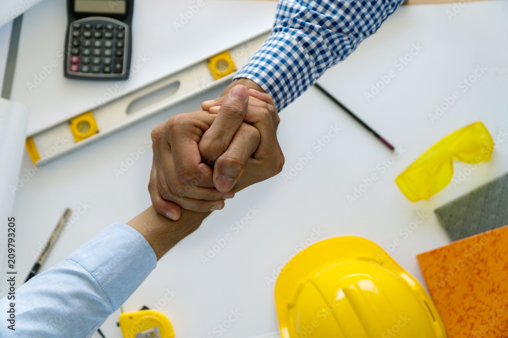 Engineer and Architect concept. Two construction engineers finished working shaking hands on table office with blueprints. Engineer and Architect concept. Two construction engineers finished working shaking hands on table office with blueprints.