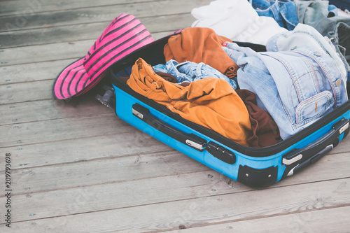 Open traveler's bag with clothing, accessories on wooden floor.