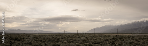 Powerlines stretch across an open valley in central California with mountains in the background under a hazy, cloudy day