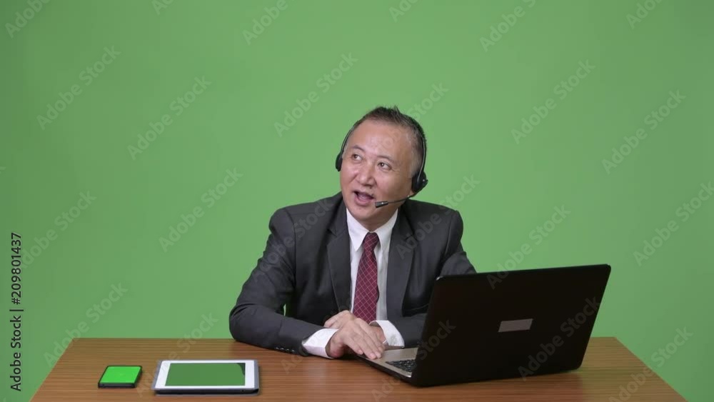 Mature Japanese businessman working as call center representative Mature Japanese businessman working as call center representative