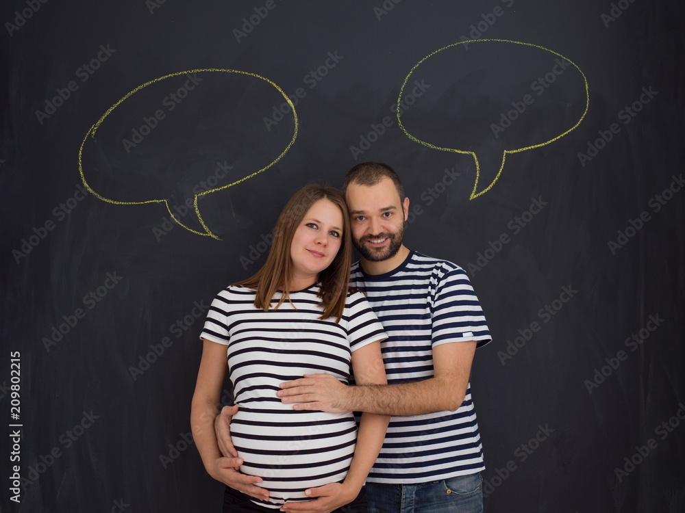 pregnant couple posing against black chalk drawing board