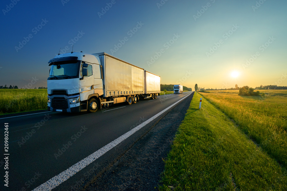 Trucks driving on the asphalt road in a rural landscape in the golden sunset