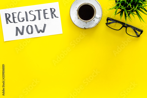 Membership concept. Template for registration. Register now hand lettering iconon word desk with glasses, coffee, plant on yellow background top view space for text photo