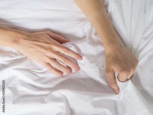 Hand clutches grasps a white crumpled bed sheet in a hotel room, a sign of ecstasy, feeling of pleasure or orgasm. Orgasm is the greatest point of sexual pleasure or a climax of sexual excitement