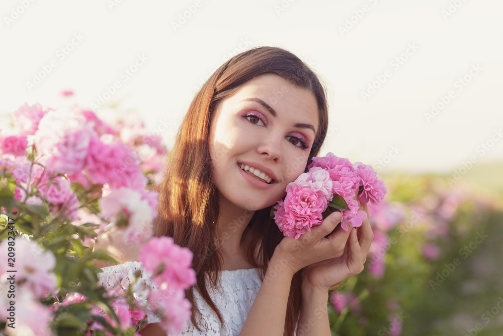 Beautiful young woman posing near roses in a garden. Beautiful young woman posing near roses in a garden.