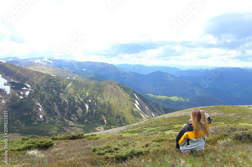 Young female tourist wearing yellow jacket standing in mountains. Concept of spending summer vacations in Alps, tourism and traveling. photo