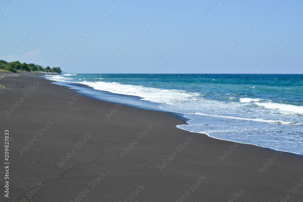 Black volcano sand beach and blue indian ocean in Bali island.