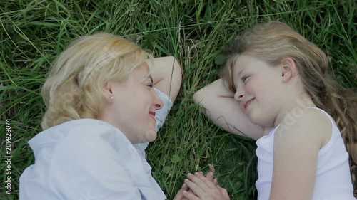 Mother and daughter lying on grass, smiling and putting their hands together. photo