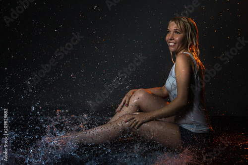 Girl in the white shirt and water drops behind and arround her illuminated by light during a photoshoot with water